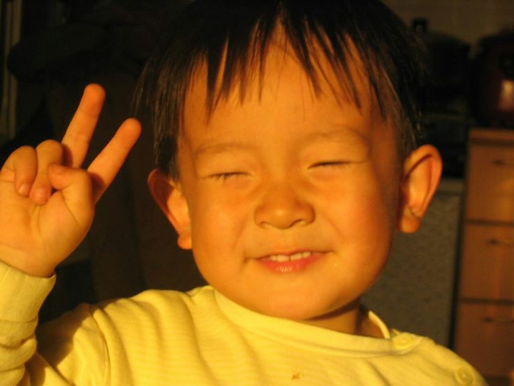 a young boy making the peace sign with his fingers in front of him and wearing a yellow shirt