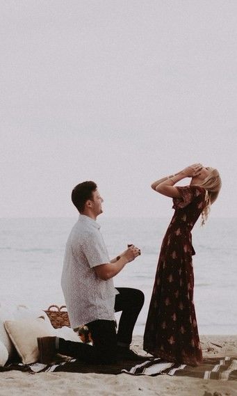 a man kneeling down next to a woman on top of a sandy beach near the ocean