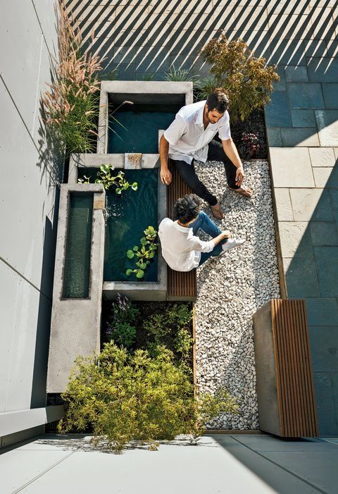 two men are standing in the middle of a small courtyard with plants and graveled walkways