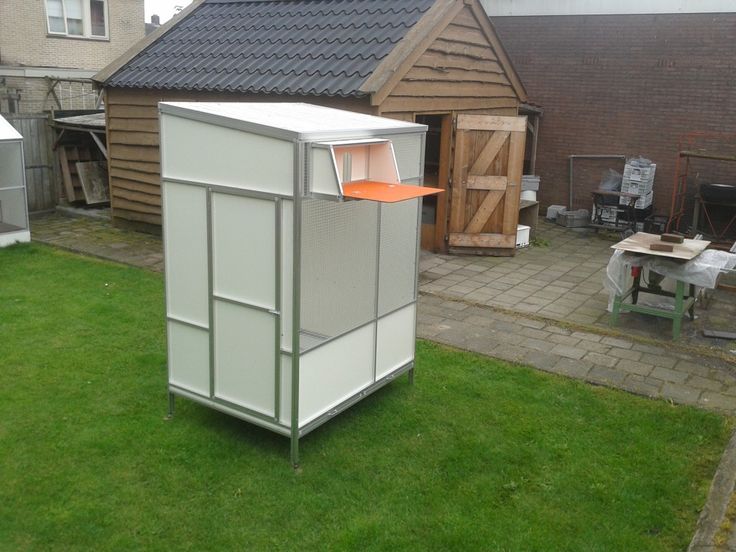 an outhouse in the middle of a yard with grass and other houses behind it