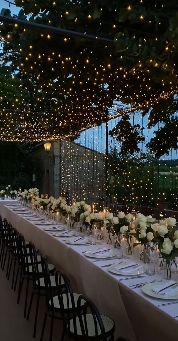 a long table is set with white flowers and lite - up lights for an outdoor event