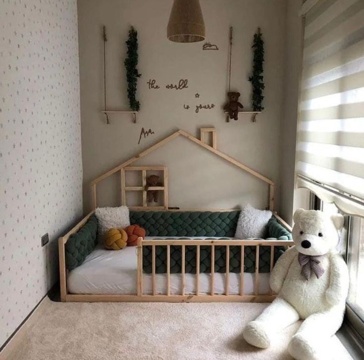 a teddy bear sitting next to a bed in a room with white walls and carpet