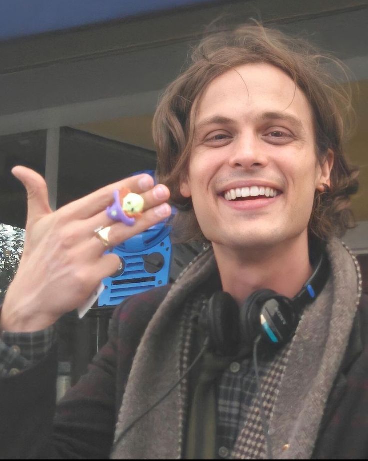 a young man smiles and holds up his peace sign while wearing headphones, scarf and jacket