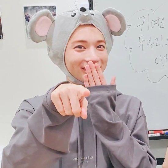 a woman wearing a mouse hat making a hand gesture with her mouth wide open while standing in front of a whiteboard