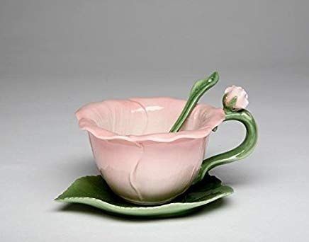 a pink flower sitting inside of a cup on top of a green leafy saucer