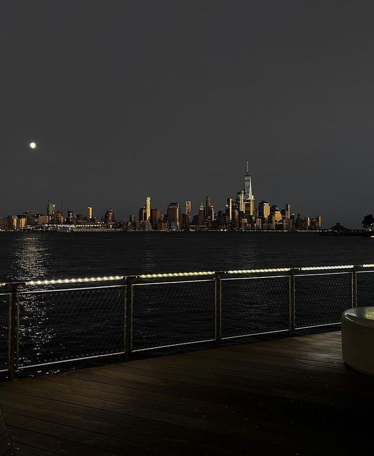 the city skyline is lit up at night as seen across the water from a pier