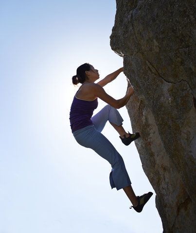 a woman climbing up the side of a rock with her hands on her hips and feet in the air