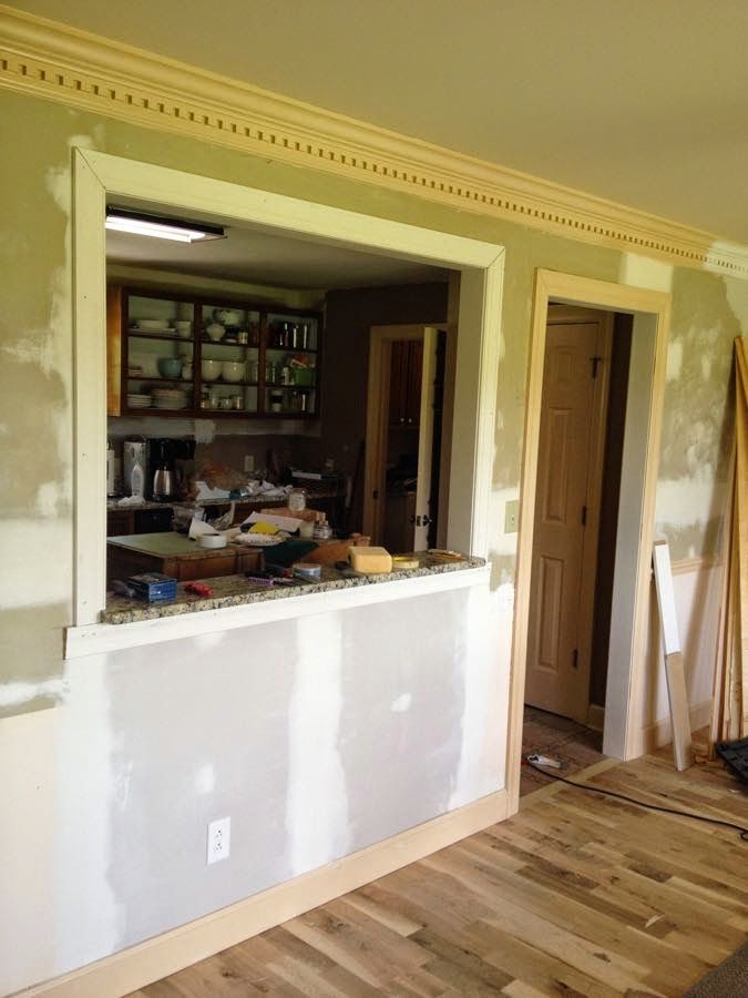 an empty room with unfinished walls and hard wood flooring in the foreground, open kitchen cabinets on the far wall