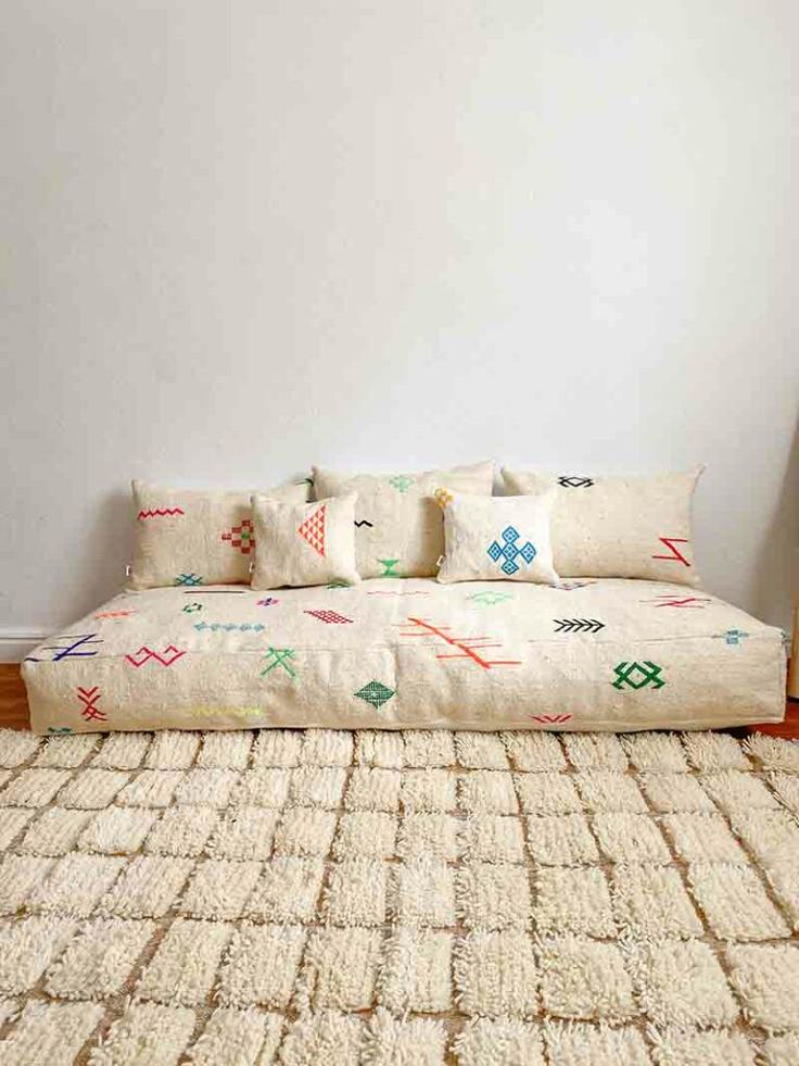 a white couch sitting on top of a wooden floor next to a rug covered in pillows