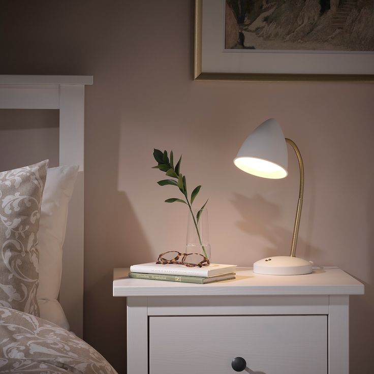 a white nightstand with a lamp and books on it in front of a pink wall