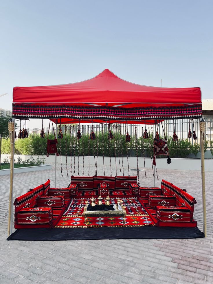 a red tent set up on top of a brick floor with chairs and rugs underneath it