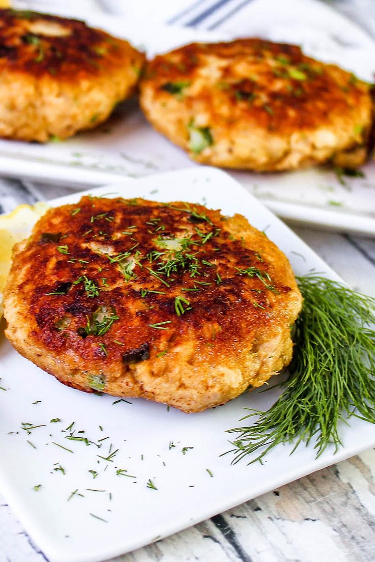 three crab cakes on a white plate with lemon wedges and parsley sprigs