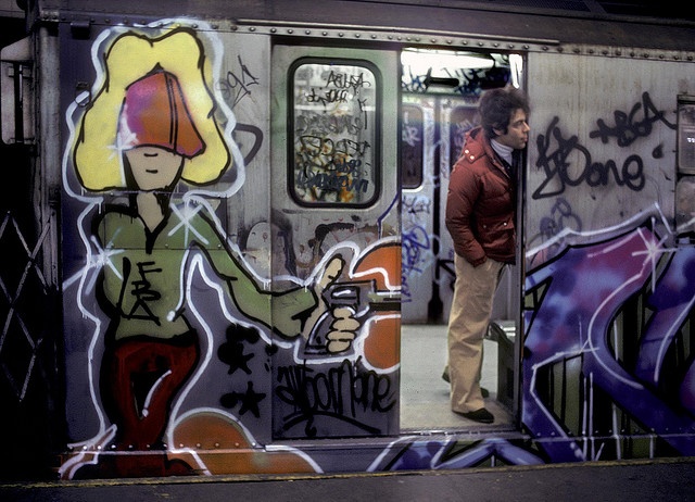 a man standing in the doorway of a subway car with graffiti on it's side