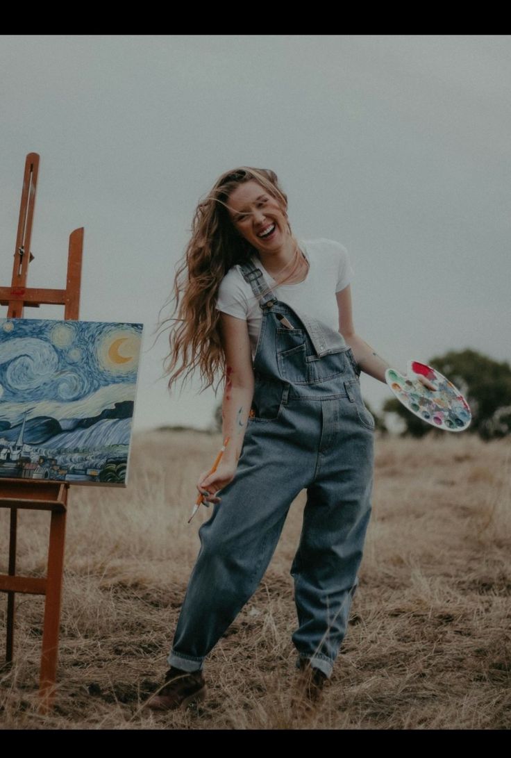 a woman standing next to an easel holding a paintbrush in her right hand