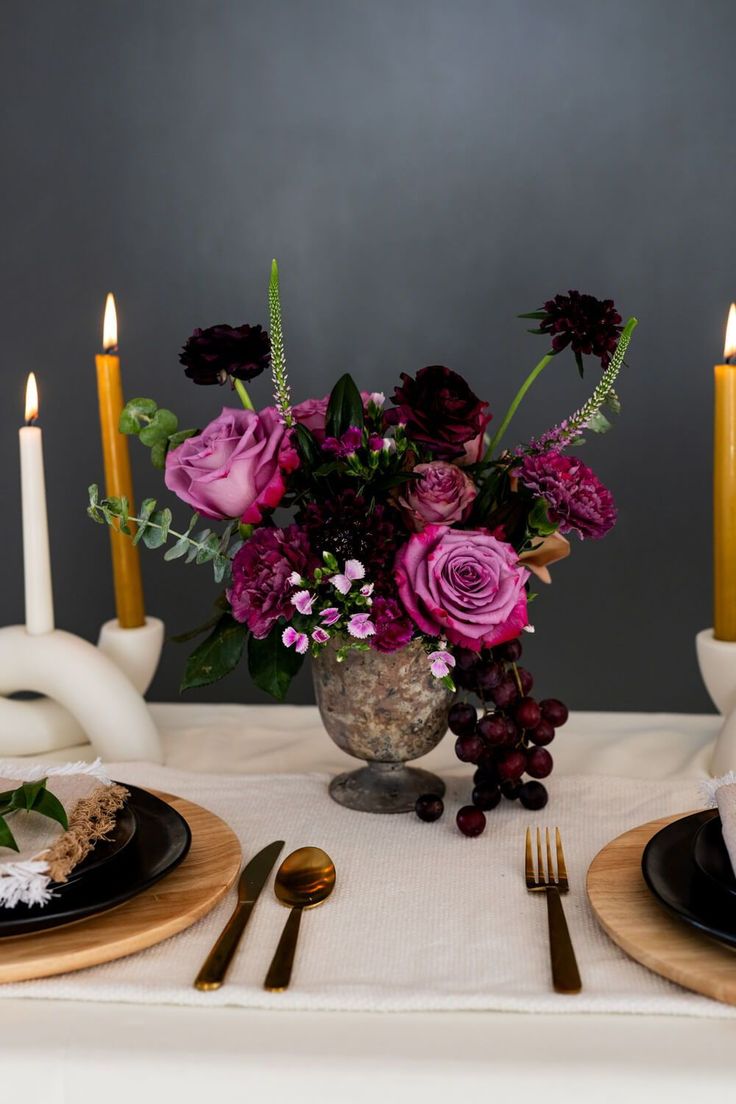 the table is set with black and white plates, silverware, and purple flowers