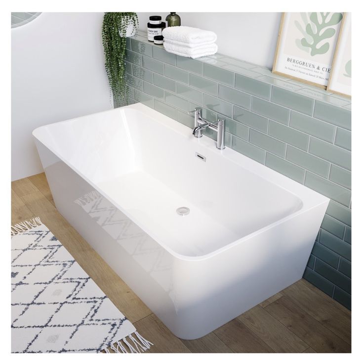 a white bathtub sitting on top of a wooden floor next to a green tiled wall