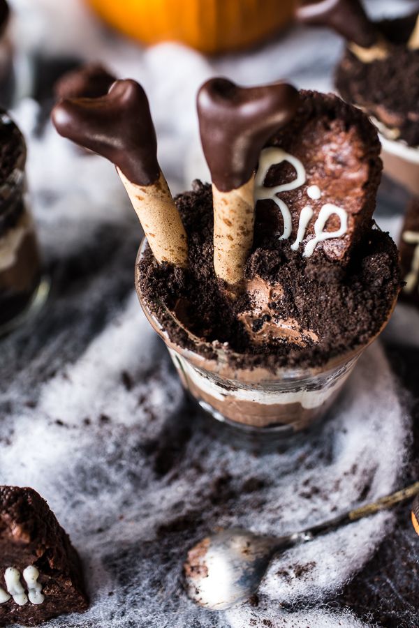 two chocolate desserts in small glass bowls with spoons on the side and halloween decorations behind them