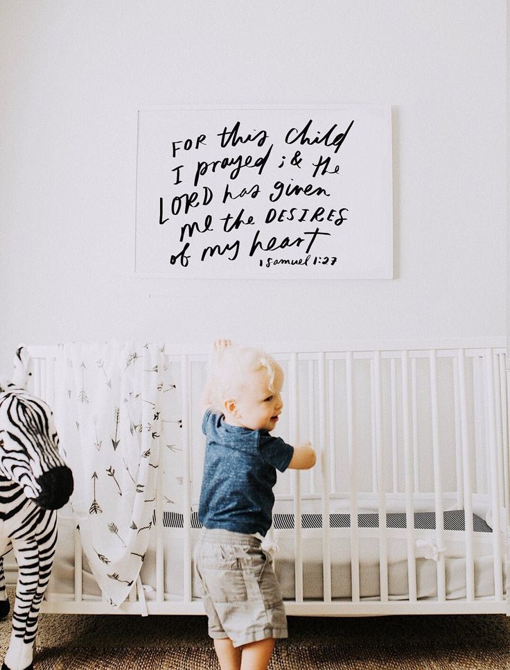 a baby standing in front of a crib with a zebra toy next to it