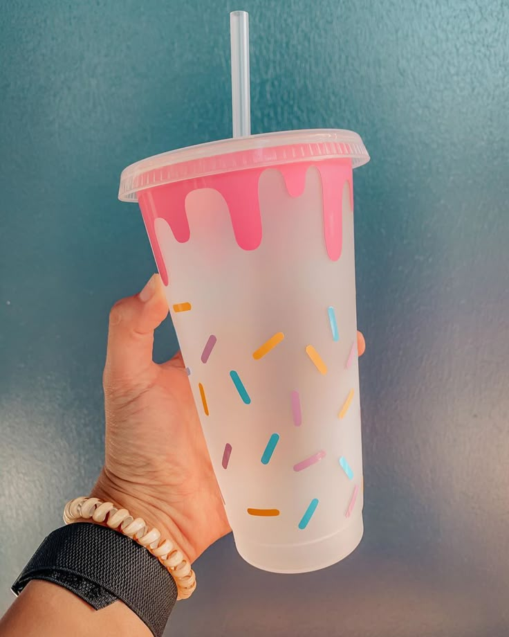 a hand holding up a plastic cup with sprinkles and a straw in it