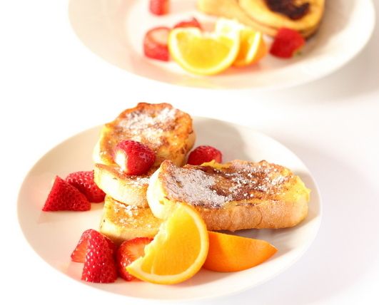 two white plates with fruit and pastries on them, one has oranges, the other has strawberries