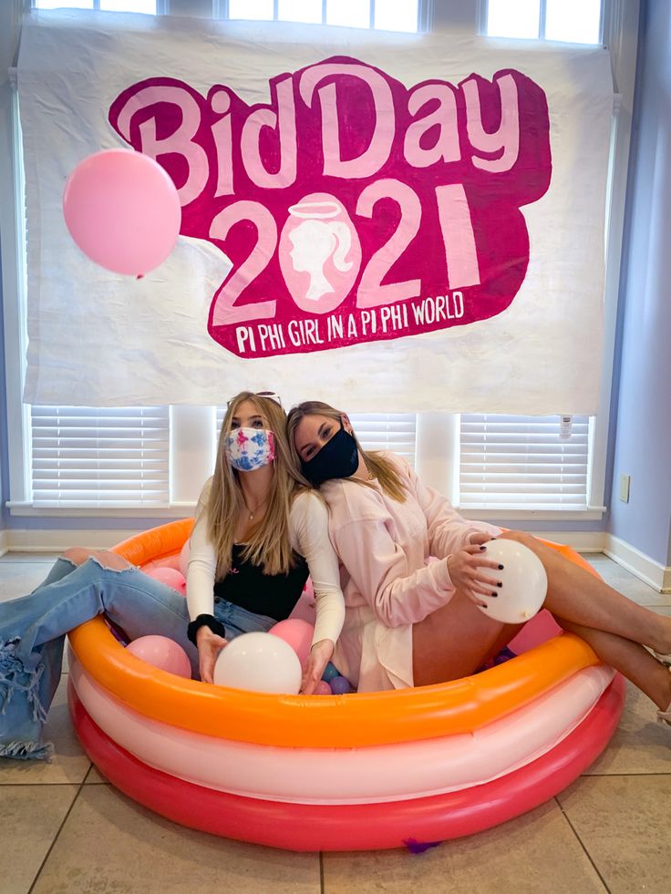 two women sitting in an inflatable pool with the words bid day on it