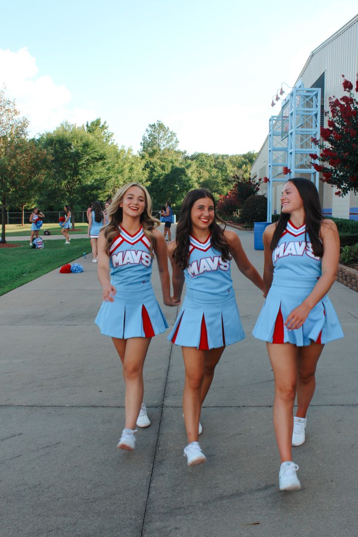 two girls in cheerleader outfits walking down the street with their hands in each other's pockets