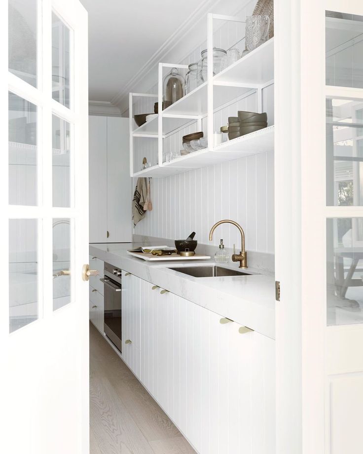 an open door leading to a kitchen with white cupboards and counter tops, along with dishes on shelves