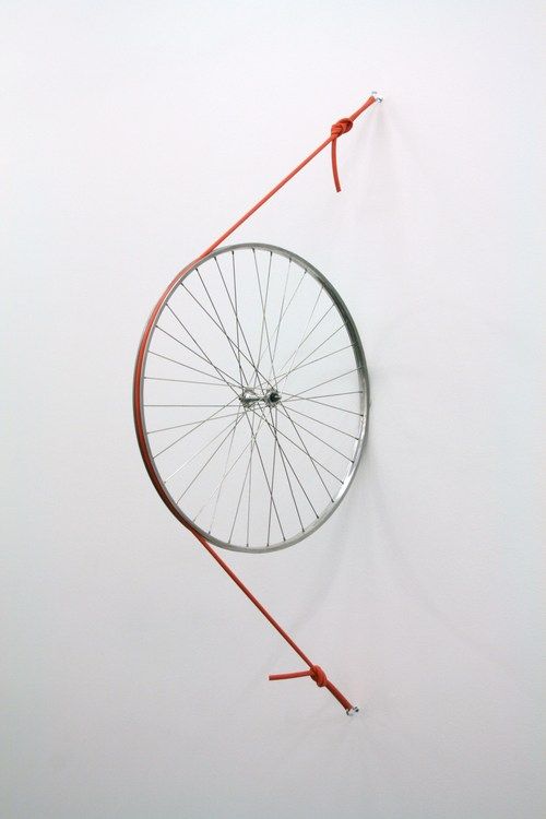 a bicycle wheel hanging on the wall with red string attached to it's side