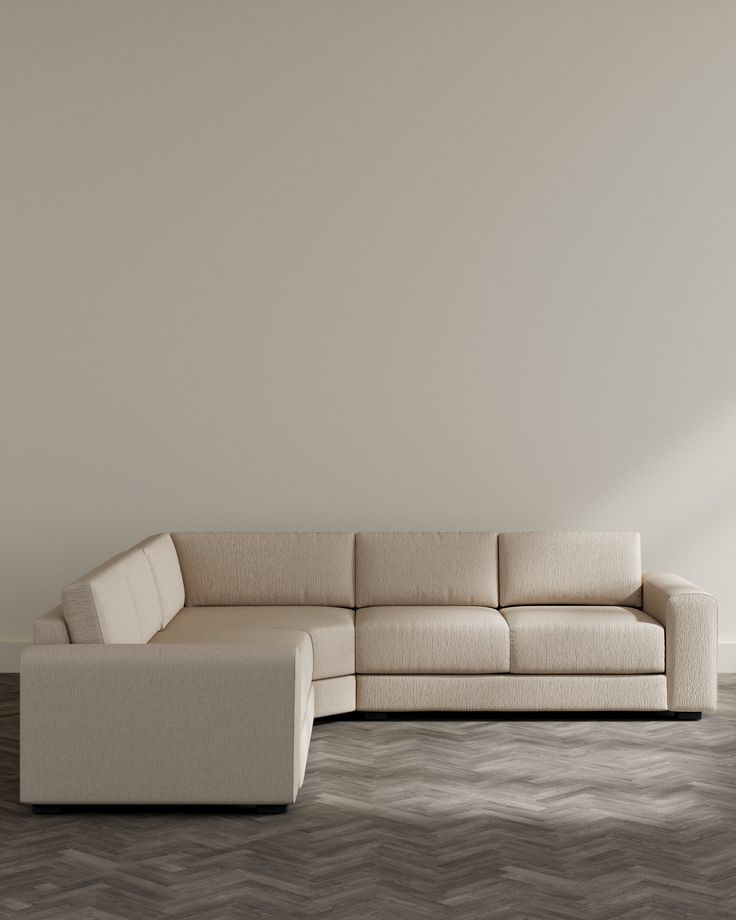 a white couch sitting on top of a hard wood floor next to a gray wall