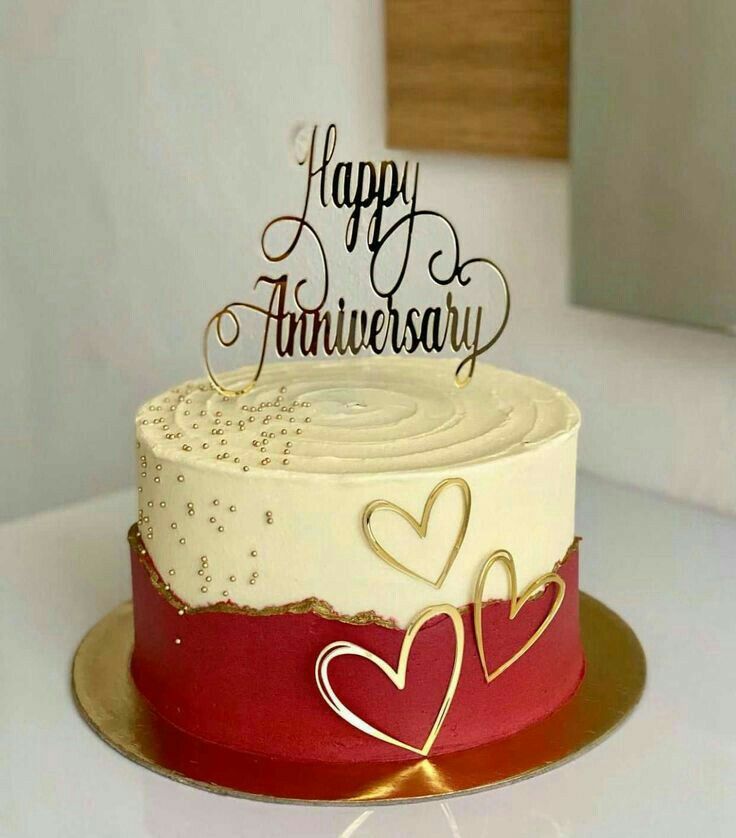 a white and red cake sitting on top of a table next to a window with the words happy anniversary written on it