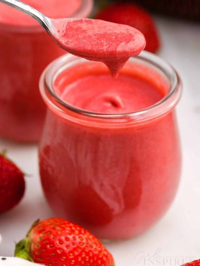 a spoon full of strawberry jam with some strawberries in the background