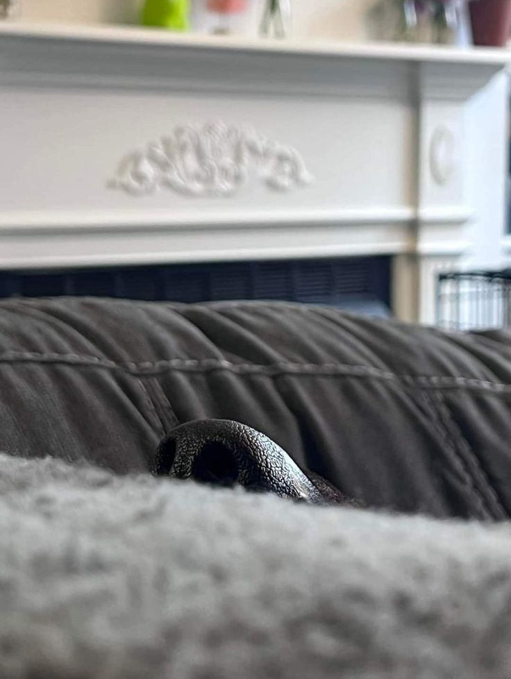 a close up of a black couch with a white fireplace in the background