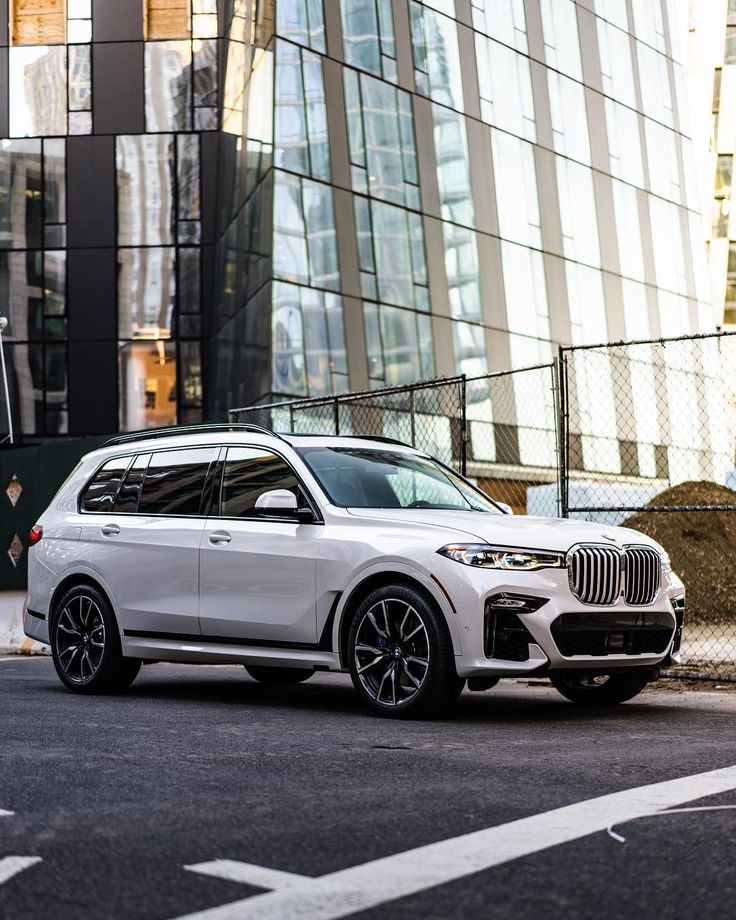 a white bmw x7 parked in front of a tall building on a city street