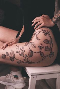 a woman sitting on top of a white stool next to a chair with tattoos on her legs