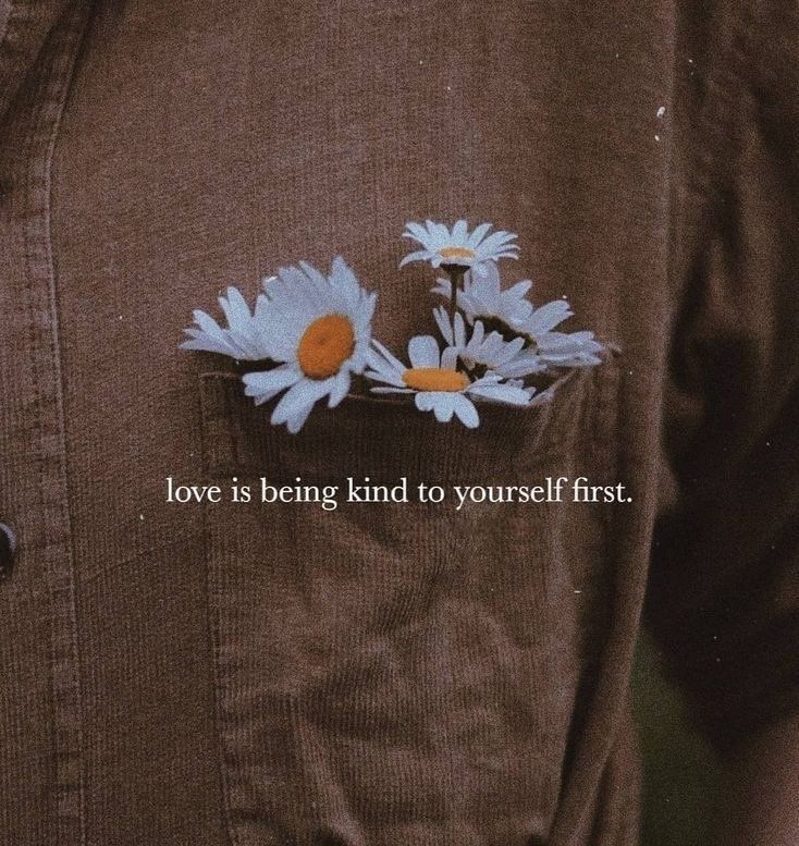 a person wearing a brown shirt with white daisies on the chest and an orange button that says love is being kind to yourself first