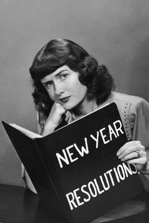 a woman sitting at a table holding up a new year resolution sign in front of her face