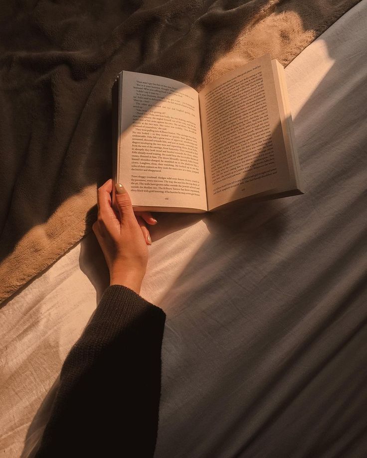 someone is reading a book on the bed with their hand resting on an open book