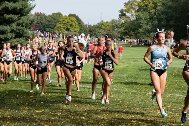 a group of women running in a cross country race on a grass field with people watching from the sidelines