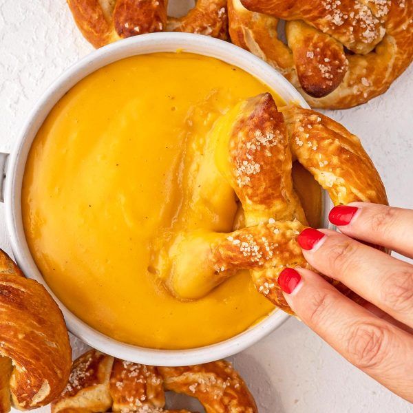 a person dipping their hand into a bowl of soup with pretzels in the background