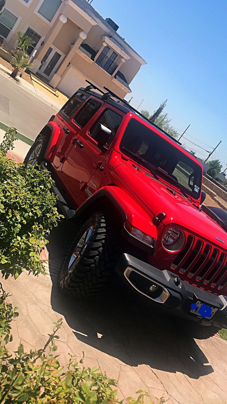 a red jeep parked on the side of a road next to a bush and building