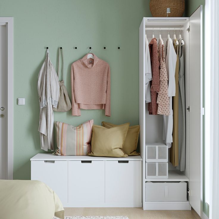 a bedroom with green walls and clothes hanging on the closet doors next to a bed