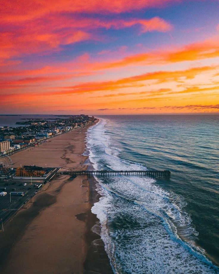 an aerial view of the beach and ocean at sunset with colorful clouds in the sky