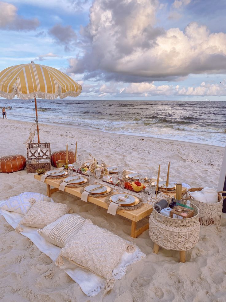 a table set up on the beach with an umbrella over it and other items laid out