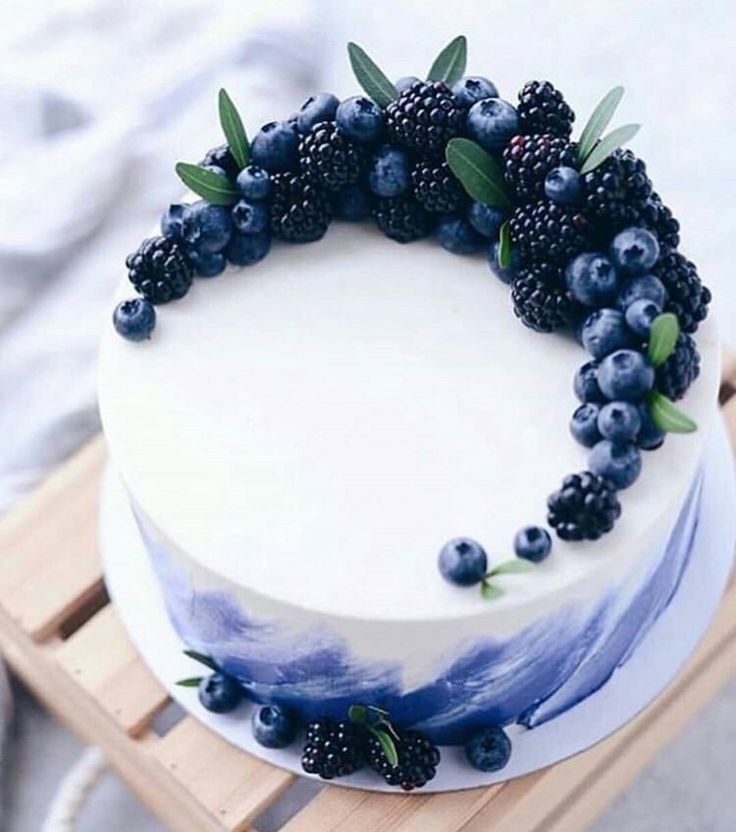 a white cake topped with blueberries and blackberries on top of a wooden tray