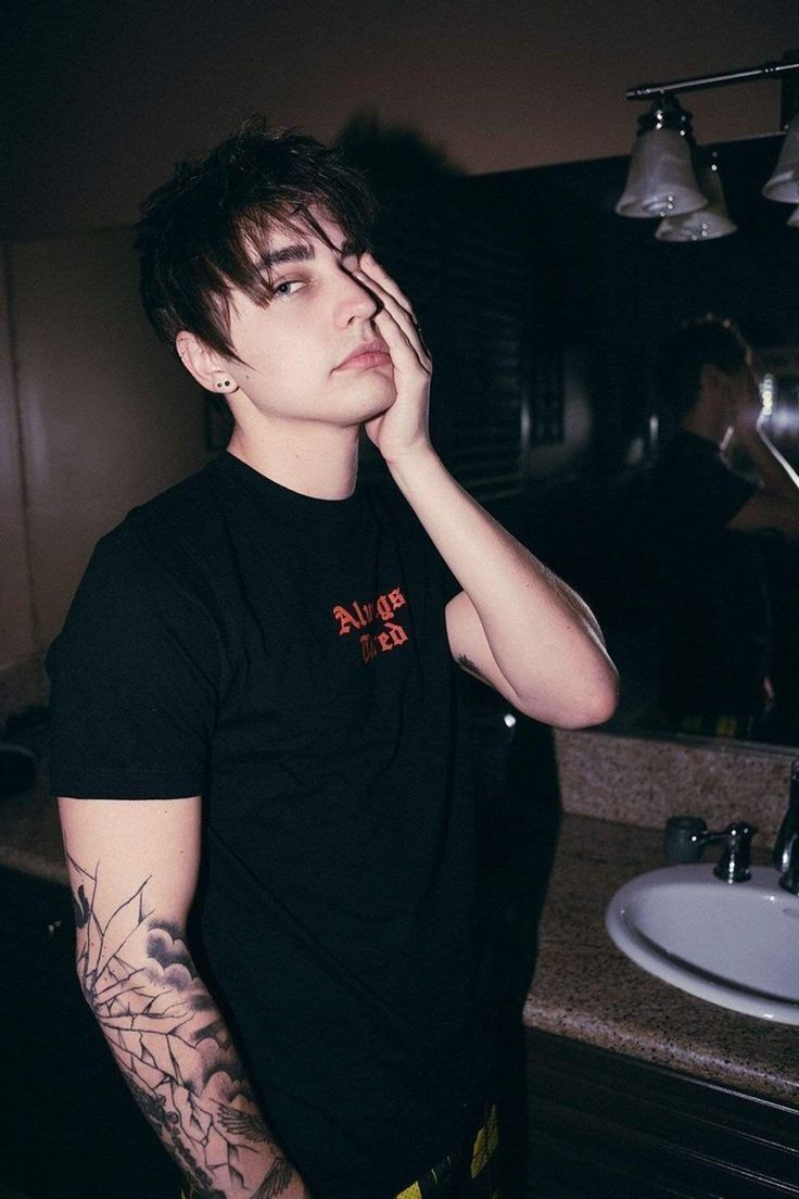 a young man with tattoos standing in front of a bathroom sink holding his hand to his face