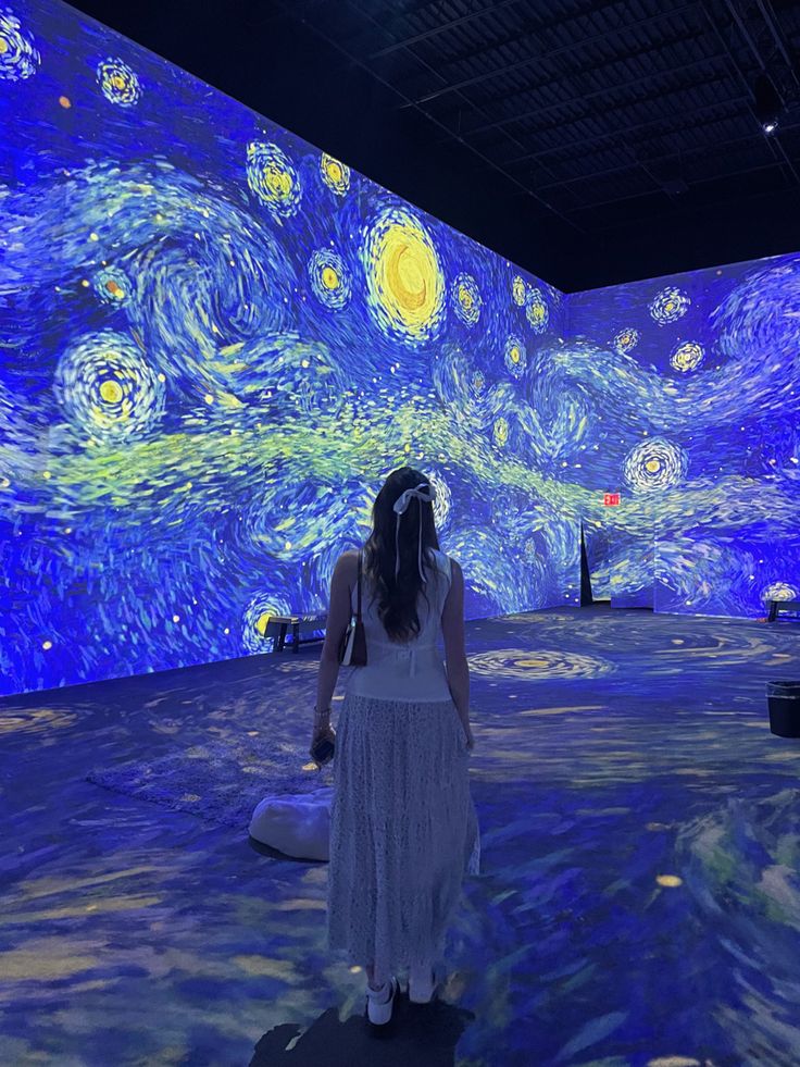 a woman standing in front of a starry night painting on the wall at an art museum