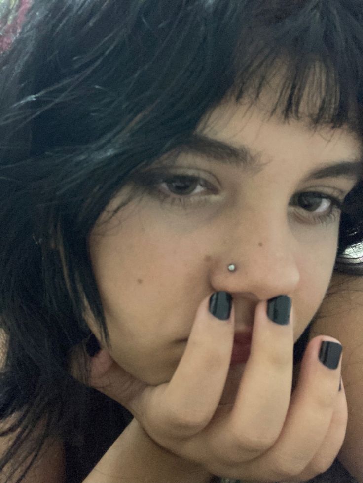 a close up of a person with black nail polish on their nails and holding her hand to her mouth