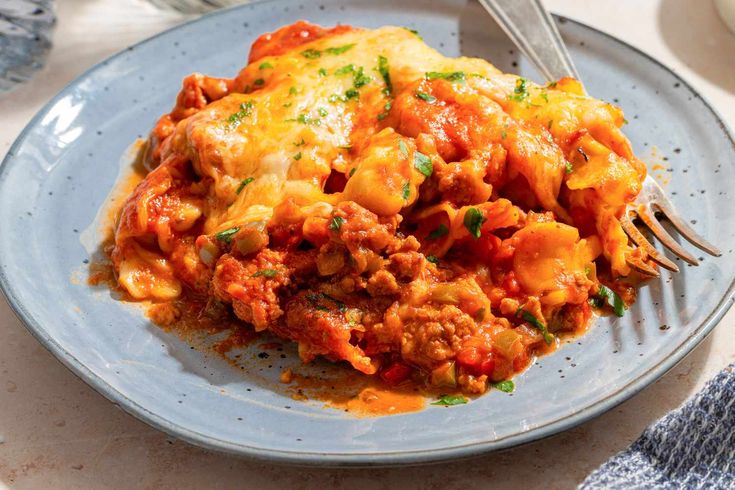 a blue plate topped with lasagna covered in sauce and cheese next to a fork