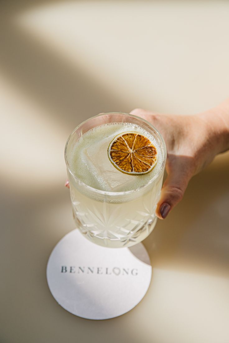 a person holding a glass with a drink in it and a slice of orange on the rim