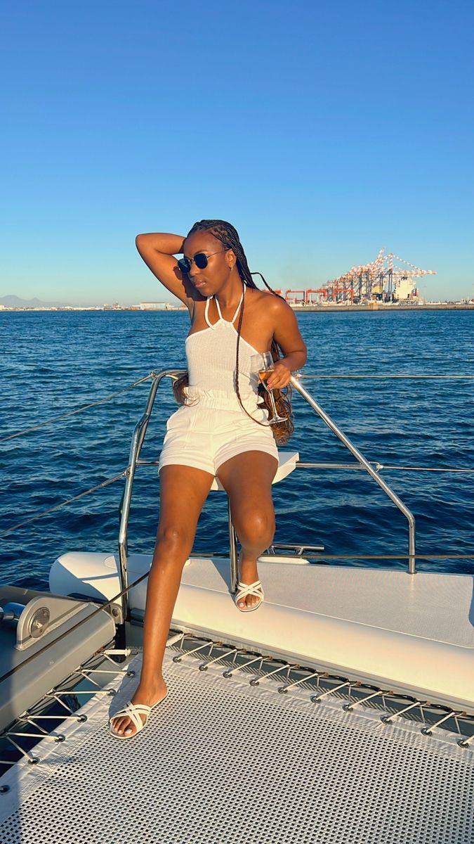 a woman sitting on the back of a boat while wearing sunglasses and a white bathing suit